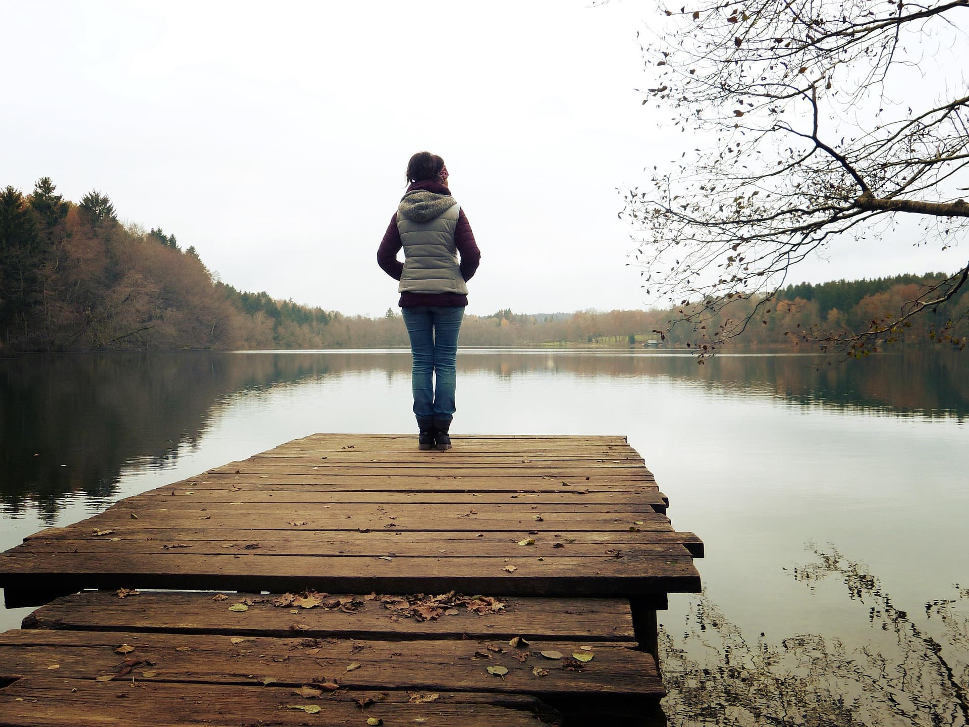 Žena stoji na drvenom molu uz mirno jezero
